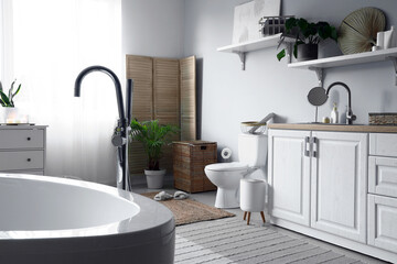 Interior of light restroom with ceramic toilet bowl, sink and vanity cabinets