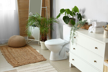 Interior of light restroom with ceramic toilet bowl, mirror and chest of drawers