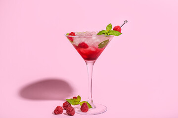 Glass of fresh raspberry mojito on pink background