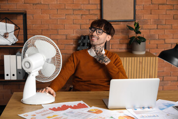 Young man with electric fan in office