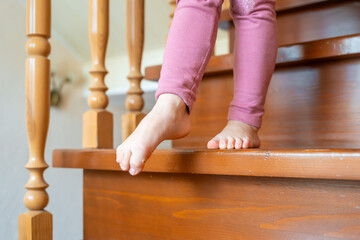 Close up of little girl feet going down the stairs at home, child climbing stairs