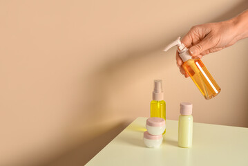 Female hand with travel cosmetic kit on table against color background