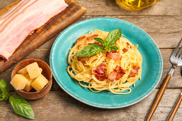 Plate with tasty pasta carbonara and ingredients on wooden background