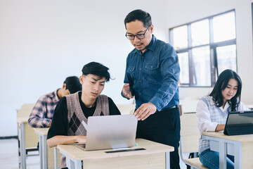 Teacher helping male student with online assignment in the classroom