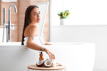 Beautiful young woman with coconut oil in bathroom