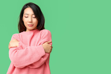 Fototapeta premium Young Asian woman hugging herself on green background