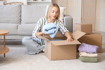 Young woman putting folded sweater in box at home