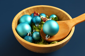Wooden bowl of salad with Christmas balls on color background, closeup