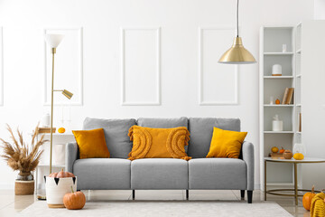 Autumn interior of living room with cozy grey sofa, standard lamp and pumpkins