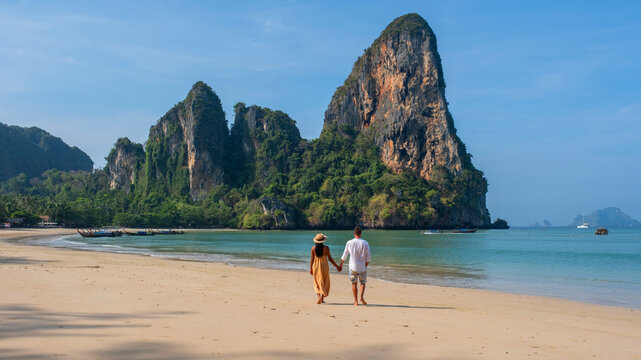 A couple of men and woman walking on the beach of Railay Beach Krabi Thailand, the tropical beach of Railay Krabi, A diverse multiracial couple walking hand in hand together on the beach