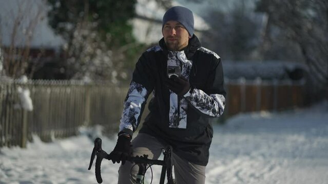 Navigation, GPS positioning, routing, offline map in a smartphone. Male cyclist stopped while cycling in winter in snow to check messages and direction of the journey. Bicycle rides in snowy weather. 