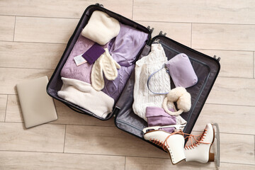 Open suitcase with winter clothes and laptop on floor, top view - obrazy, fototapety, plakaty