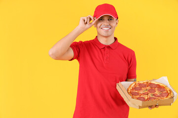 Male courier with tasty pepperoni pizza on yellow background