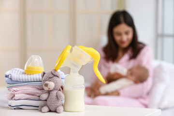 Breast pump with baby clothes and toy on table in bedroom, closeup