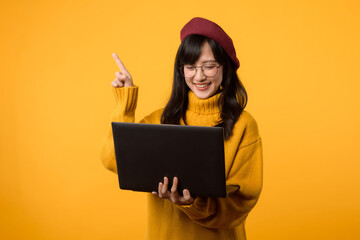 Smiling female executive in a stylish yellow setting, pointing to free copy space on her laptop...