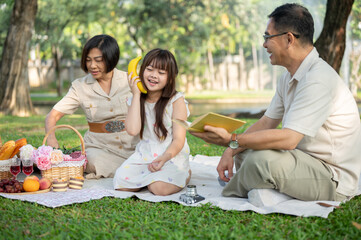 A playful Asian girl is enjoying playing and picnicking with her grandparents in the green park.
