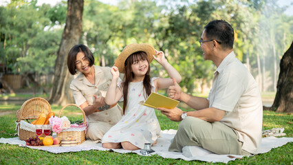 Kind and happy Asian grandparents are enjoying a picnic with their cute granddaughter in a park.