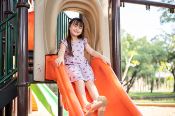 A playful and happy young Asian girl is on a colorful slide and enjoying playing in a playground.