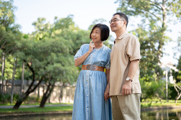 Happy retired senior Asian couples are strolling around a public park on the weekend together.