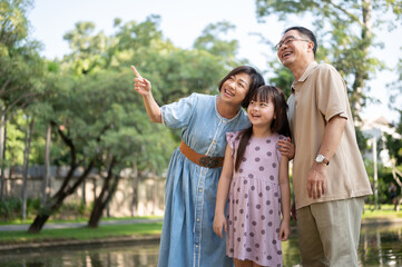 Kind Asian grandparents are having fun with their granddaughter, strolling around the park together.