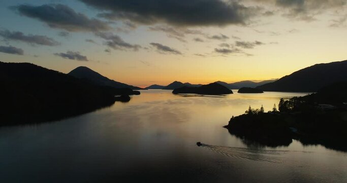 Aerial view of small boat traveling through golden sunlight and silhouetted peninsulas in Elaine bay in Pelorus Sound Te Hoiere of Marlborough Sounds, South Island of New Zealand Aotearoa