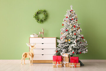 Beautiful Christmas tree with gift boxes and chest of drawers near green wall