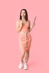 Beautiful young sporty woman with measuring tape and cutlery on pink background. Weight loss concept
