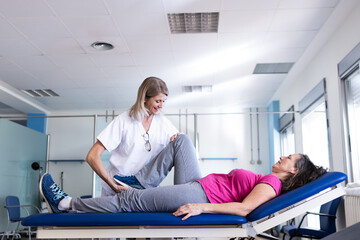 A middle aged blonde physiotherapist is rehabilitating her patient who is a brunette woman with leg problems.