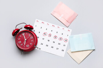 Composition with menstrual calendar, feminine hygiene products and alarm clock on grey background