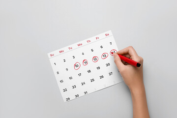 Woman marking her period in menstrual calendar on grey background