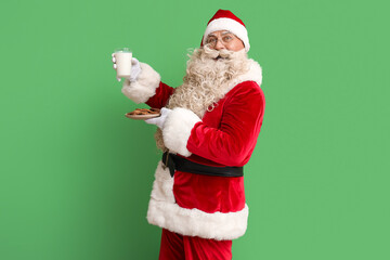 Fototapeta na wymiar Santa Claus with glass of milk and tasty cookies on green background