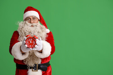 Santa Claus with alarm clock on green background