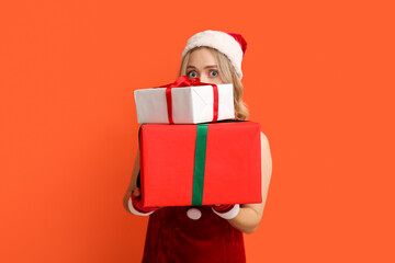 Beautiful young woman dressed as Santa Claus with Christmas gifts on orange background