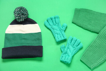 Knitted warm gloves, hat and sweater on green background