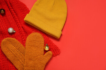 Knitted mittens, warm hat, scarf and Christmas balls on red background