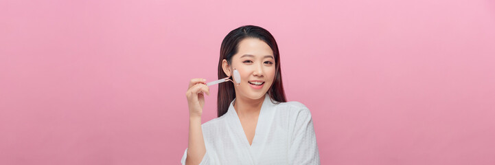 Beauty portrait of a young woman with smooth fresh skin using a jade roller for a facial massage in...
