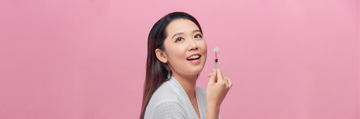 Beautiful asian woman massaging face with jade roller isolated on pink background