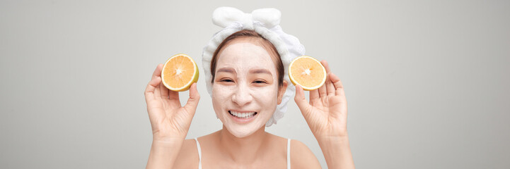 portrait of pretty young woman with clay mask on her face holding slices of orange - 678490953