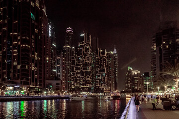 Night view from the promenade of Dubai Marina with illuminated skyscrapers, a water channel, yachts...