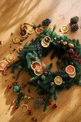 Christmas wreath surrounded by pieces of dried fruit and cones lies on a wooden floor. Top view
