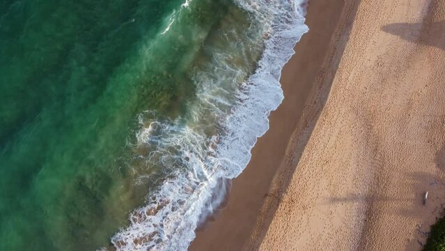 Aerial top down view over clear, transparent ocean water foaming at the shore. Sunset sun enlightens the gorgeous tropical nature of Hawaii, Kauai island, Donkey beach,  USA 4K.