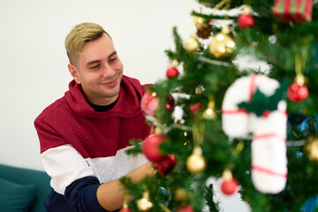 young man decorating Christmas tree at home