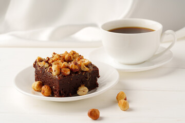 Piece of brownie cake with hazelnuts on white background