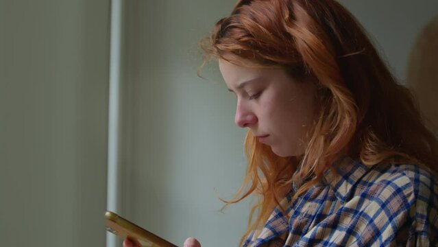 A red-haired girl scrolling social media on smartphone 