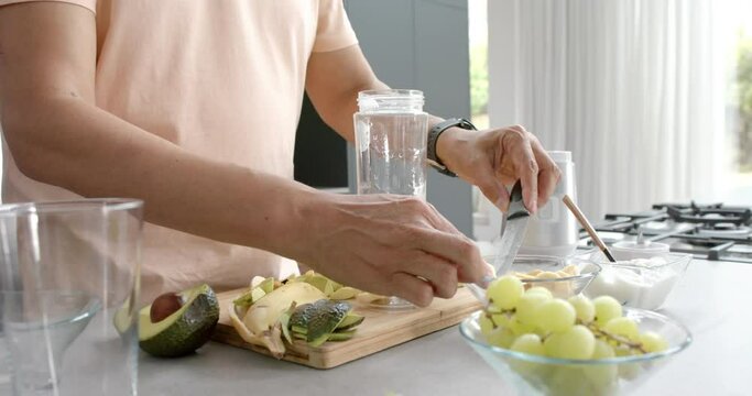 Midsection of senior biracial man preparing healthy smoothie in kitchen at home, slow motion