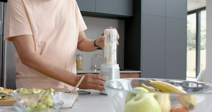 Midsection of senior biracial man blending healthy smoothie in kitchen, copy space, slow motion