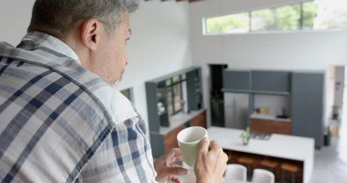 Happy senior biracial man drinking coffee on upstairs landing at home, copy space, slow motion