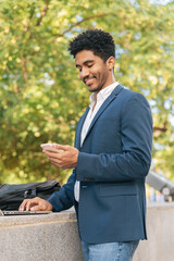 Fototapeta premium Cheerful ethnic man with smartphone and laptop