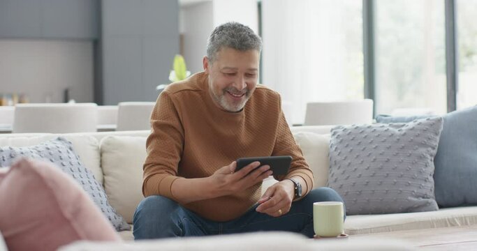 Happy senior biracial man having smartphone video call on couch in sunny living room, slow motion