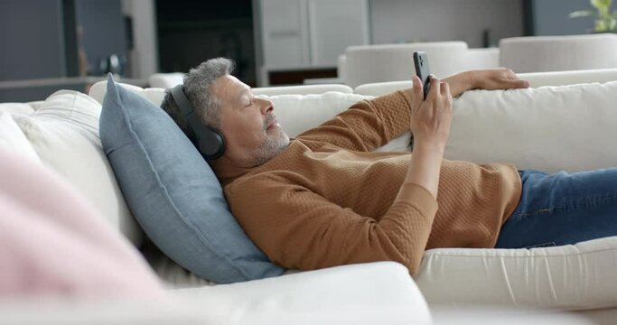 Senior biracial man on couch in headphones listening to music on smartphone, copy space, slow motion